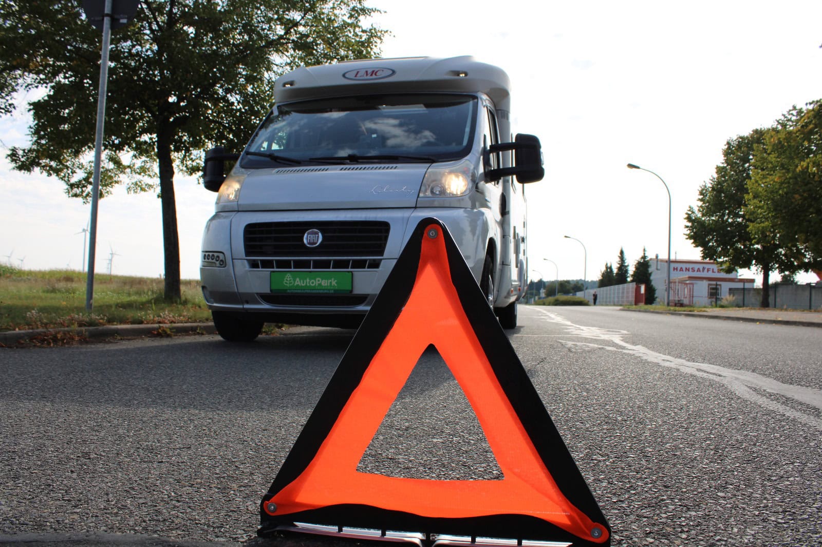 Frontansicht eines Wohnmobils auf der Straße. Vor dem Fahrzeug steht ein Warndreieck.